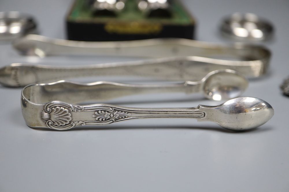 Small silver including a pair of Georgian sugar tongs, cased pepperettes, two napkin rings, spoon, tongs and wine label.